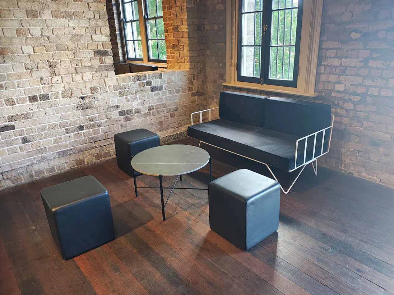 Modern lounge furniture setup with black leather ottoman cubes, round coffee table and black sofa against exposed brick walls