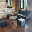 Modern lounge furniture setup with black leather ottoman cubes, round coffee table and black sofa against exposed brick walls