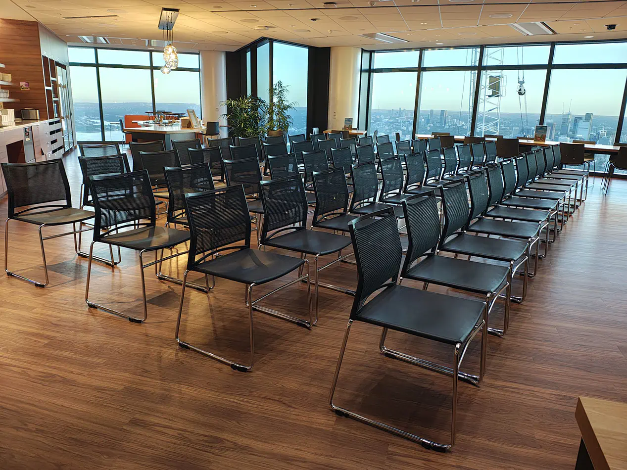 Black mesh conference chairs arranged in rows inside a modern function room with timber flooring and large windows overlooking the city skyline
