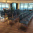 Black mesh conference chairs arranged in rows inside a modern function room with timber flooring and large windows overlooking the city skyline