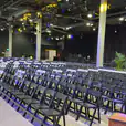 A large auditorium with rows of black padded folding chairs and lights.