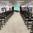 A large conference room with rows of chairs, including black padded folding chairs, and a projector.