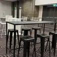 A room with black rectangular tables and stools in it.