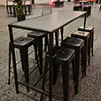 Black rectangular tapas table with industrial black stools positioned inside a large contemporary corporate event venue