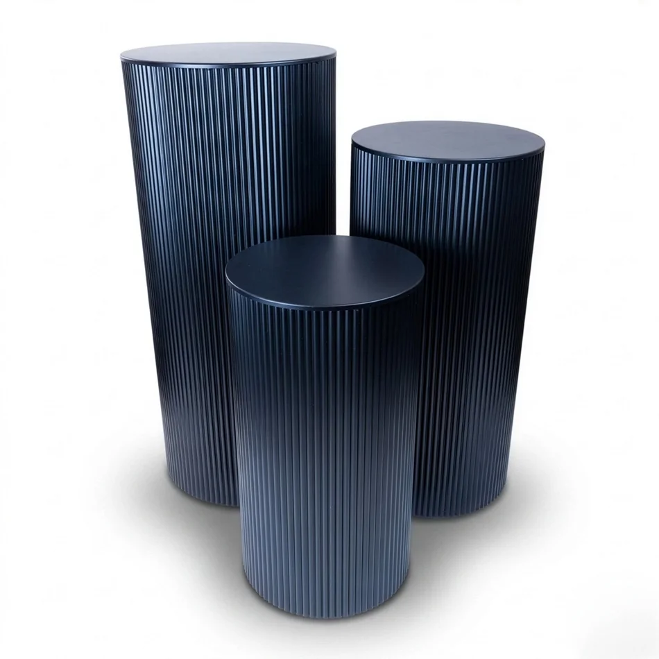 Three black ripple metal plinths with round tops and fluted sides in graduated heights