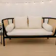 Black round side table styled beside a rattan lounge with cream cushions, set on a woven rug with soft decorative lighting for an elegant event seating setup.