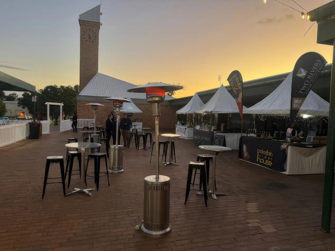 Black tolix stool hire arranged around cocktail tables at an outdoor evening festival with market stalls, heaters and ambient lighting