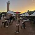 Black tolix stool hire arranged around cocktail tables at an outdoor evening festival with market stalls, heaters and ambient lighting