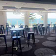 Black tolix stool hire setup inside a bright function room with round cocktail tables, large windows and chandelier lighting overlooking coastal views