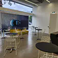 Black top cocktail tables paired with white wire chairs in a modern showroom event space with large windows, polished concrete floor, and contemporary interior design
