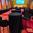 Black velvet bar stools with curved padded backs positioned around black linen cocktail tables at a university conference showcase