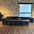 Black velvet bench seating with matching velvet ottomans and round wire coffee table in a warehouse-style event lounge with exposed brick walls