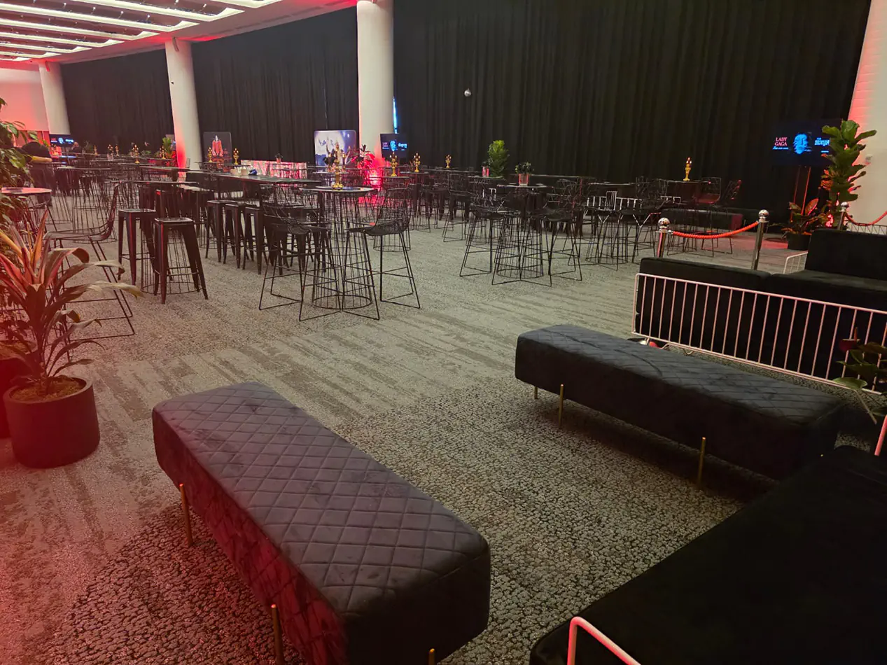 Black velvet bench seating combined with wire bar furniture and cocktail tables inside a large premium event venue with ambient lighting