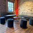 Black velvet cylinder stools with wire lounge seating and round coffee table inside an industrial-style event venue with exposed brick walls