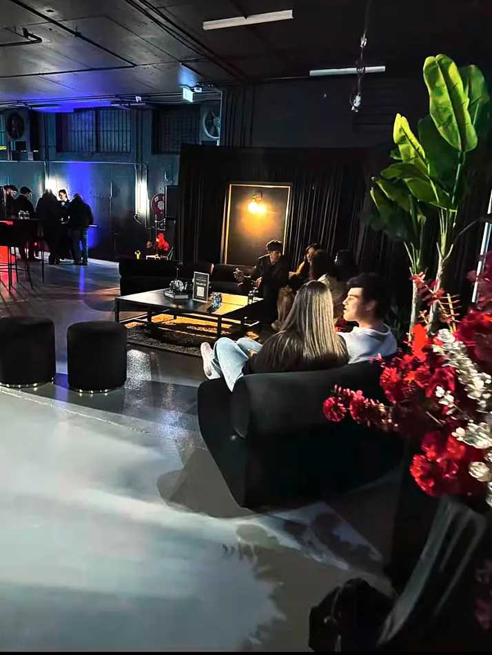 Black velvet ottoman stools with gold bases in a black draped lounge area at an evening event.