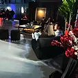 Black velvet ottoman stools with gold bases in a black draped lounge area at an evening event.