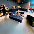 Black velvet ottoman benches arranged in an L around a gold coffee table and black and gold rug in a car showroom.