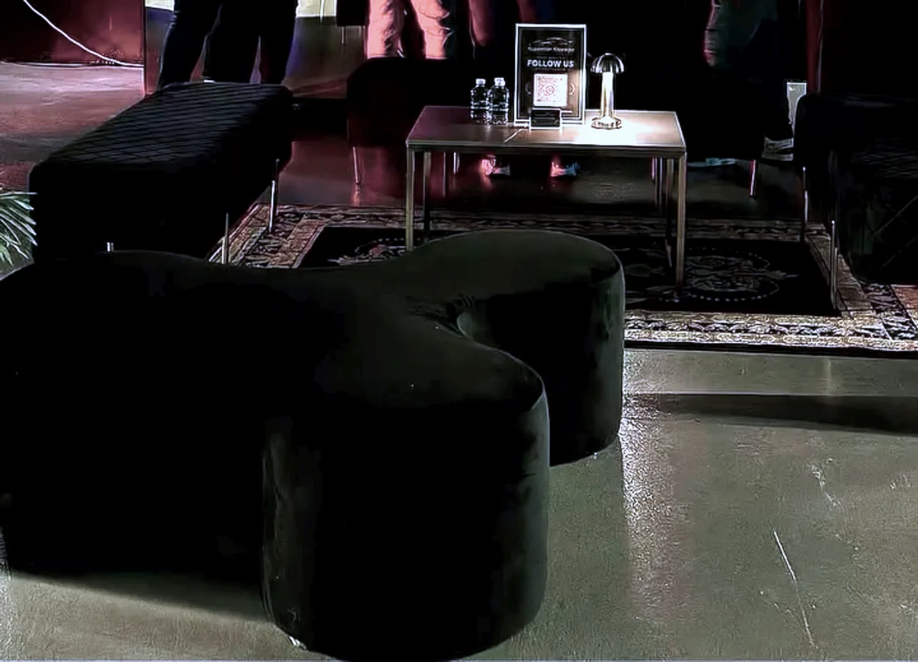 Black velvet ottoman benches either side of a gold coffee table and ornate rug in a supercar showroom lounge.