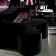 Black velvet ottoman benches either side of a gold coffee table and ornate rug in a supercar showroom lounge.