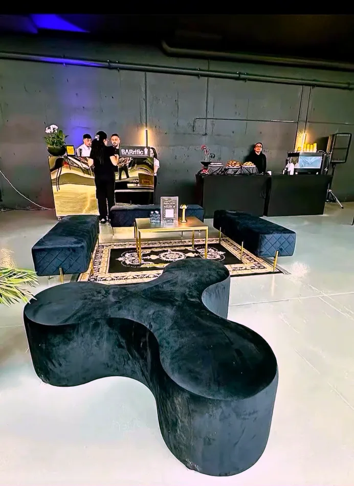 Black velvet ottoman benches framing a black and gold rug in a warehouse event space.