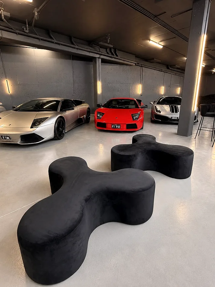 Two black velvet Apollo tripod daybeds arranged as feature seating in a supercar showroom.