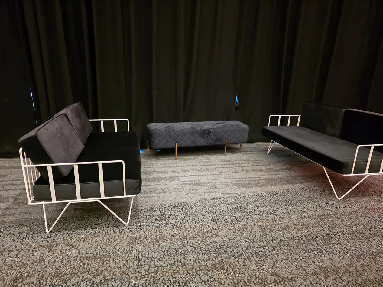 Black velvet wire lounge sofas with quilted ottoman bench arranged in front of black draped walls at an indoor event venue