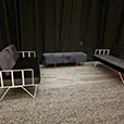 Black velvet wire lounge sofas with quilted ottoman bench arranged in front of black draped walls at an indoor event venue