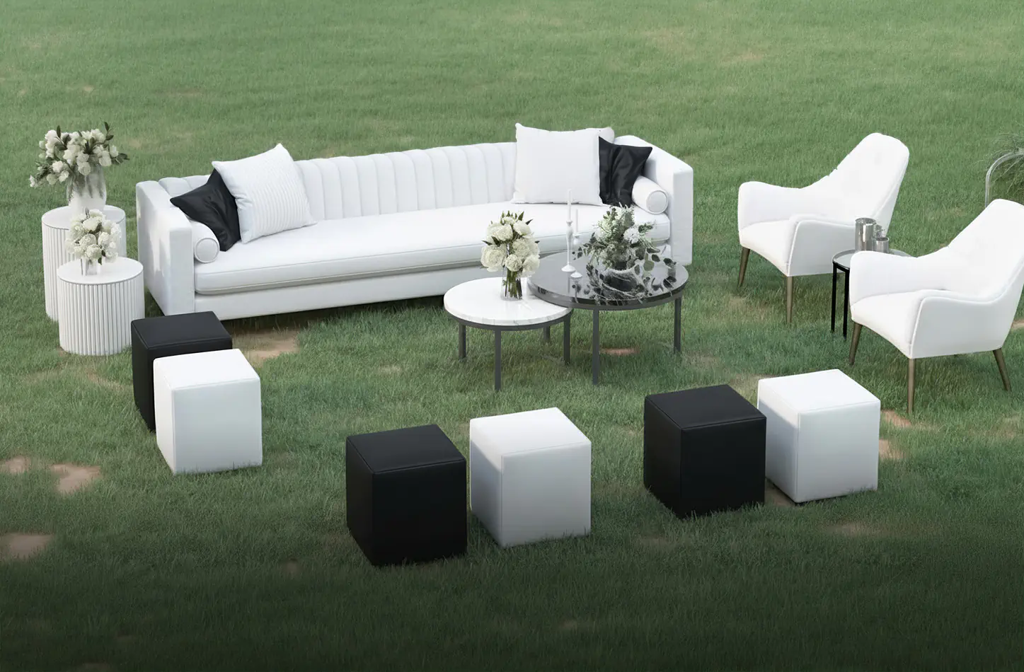 Outdoor event lounge setup featuring black and white ottoman cube seating arranged on grass around white sofas and round coffee tables