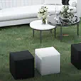 Outdoor event lounge setup featuring black and white ottoman cube seating arranged on grass around white sofas and round coffee tables