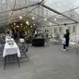 A clear tent with tables and black wire chairs in it.
