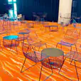 A room with chairs and tables on an orange floor, including Black Wire Chairs or Black Arrow Chair Hire options.