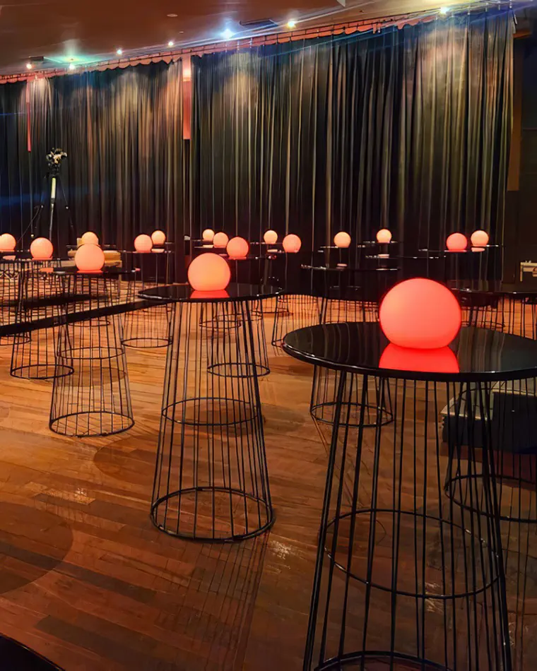 Black wire cocktail table hire arranged across an event space with warm ambient lighting, glowing centrepieces and draped backdrop