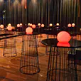 Black wire cocktail table hire arranged across an event space with warm ambient lighting, glowing centrepieces and draped backdrop