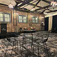 Black wire cocktail table hire with matching seating in a modern function room featuring exposed brick walls, stage area and overhead lighting