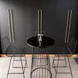 Black wire cocktail table with a gloss black top flanked by two black wire bar stools against a dark panelled wall