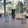 Black wire cocktail tables spaced throughout a bright corporate venue with large windows, polished floors and display setup for an event