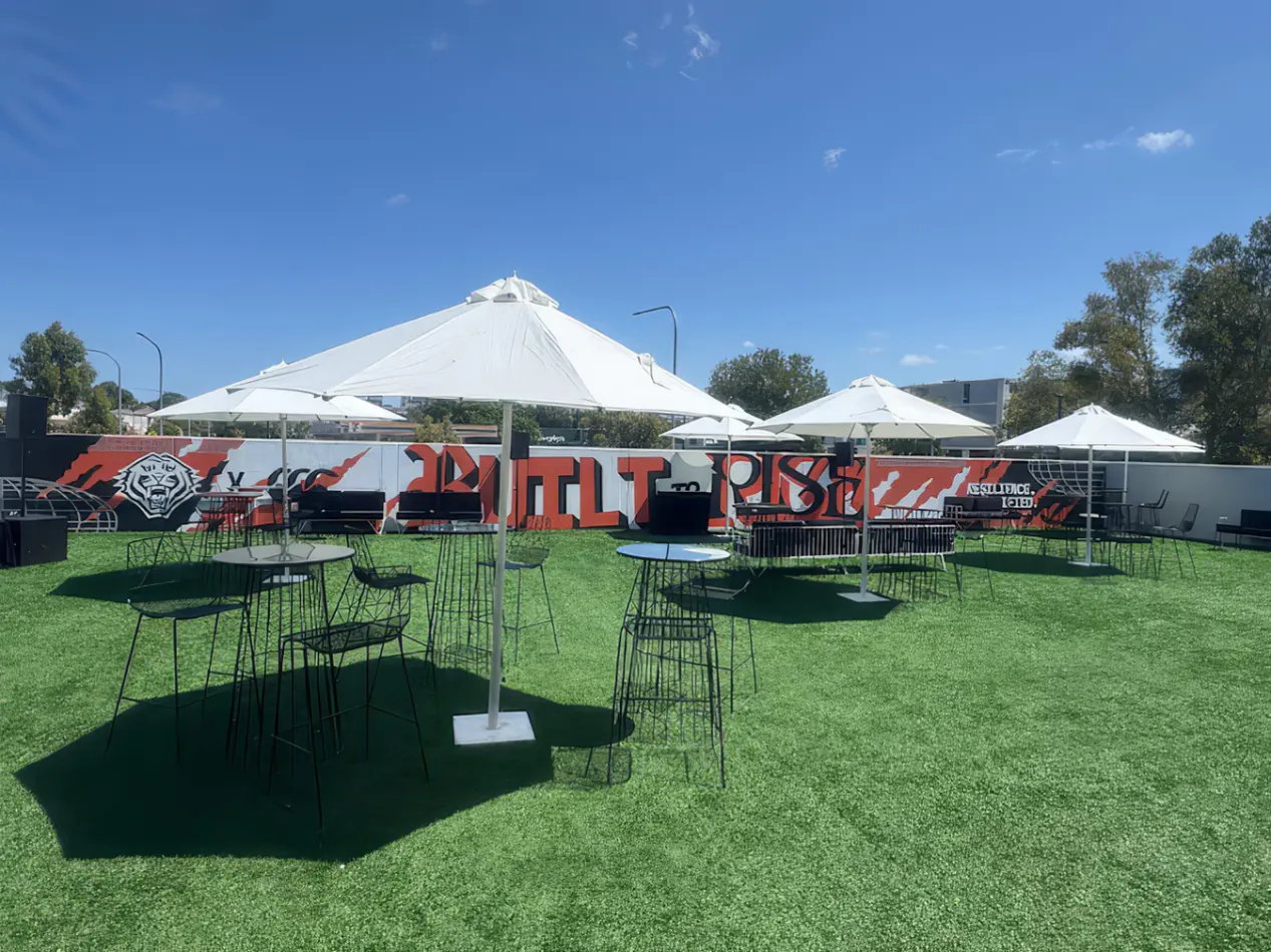 Black wire stools with round cocktail tables set on outdoor grass area under white umbrellas at an event venue