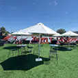 Black wire stools with round cocktail tables set on outdoor grass area under white umbrellas at an event venue