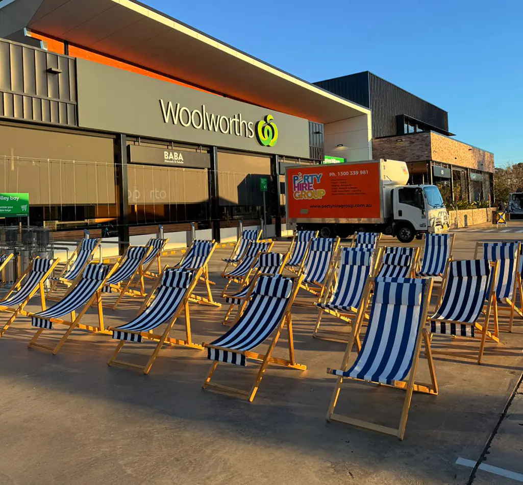 Blue and white striped deck chairs arranged outdoors for a community event beside a shopping precinct at sunset