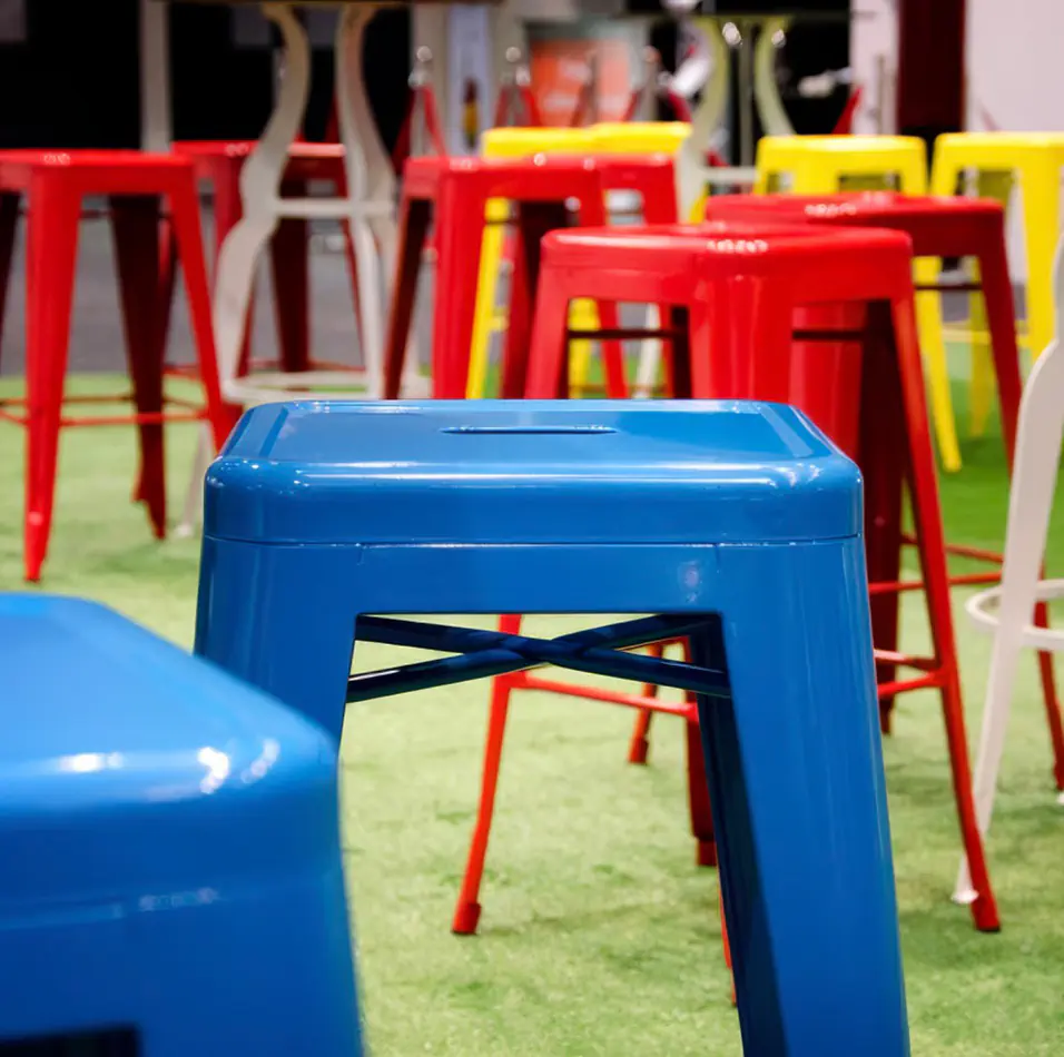 Close-up of blue tolix stool hire with other colourful stools in the background on artificial grass flooring, suitable for casual event seating