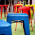 Close-up of blue tolix stool hire with other colourful stools in the background on artificial grass flooring, suitable for casual event seating