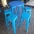 Blue tolix stools arranged around a matching cocktail table in an indoor event space with plants and bar setup in the background