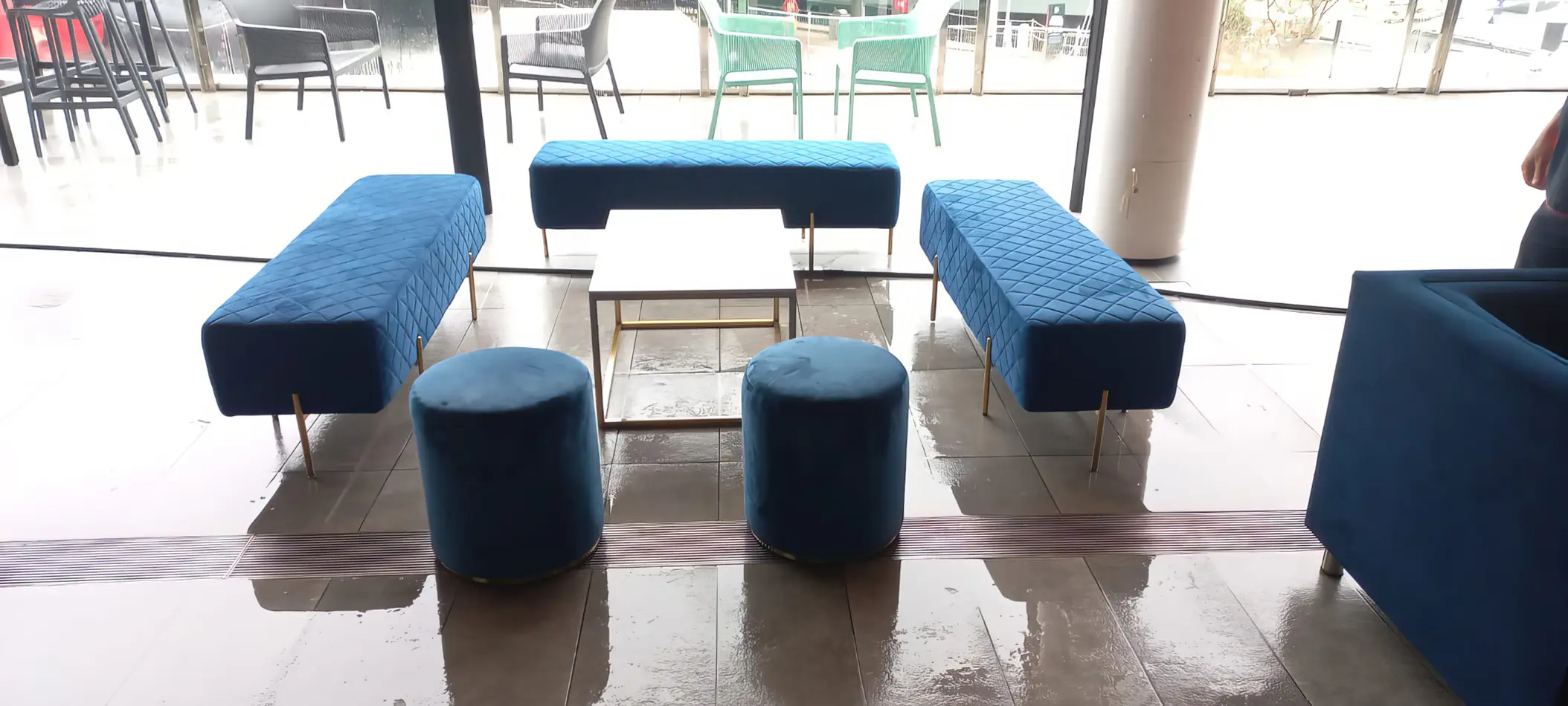 Blue velvet lounge seating with benches, ottomans and a central coffee table arranged in a modern indoor event space with tiled flooring