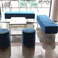 Blue velvet lounge seating with benches, ottomans and a central coffee table arranged in a modern indoor event space with tiled flooring