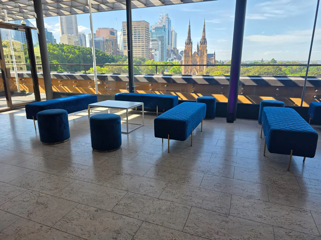 Blue velvet ottoman bench seating with matching stools and sofas in a modern event lounge overlooking the Sydney skyline
