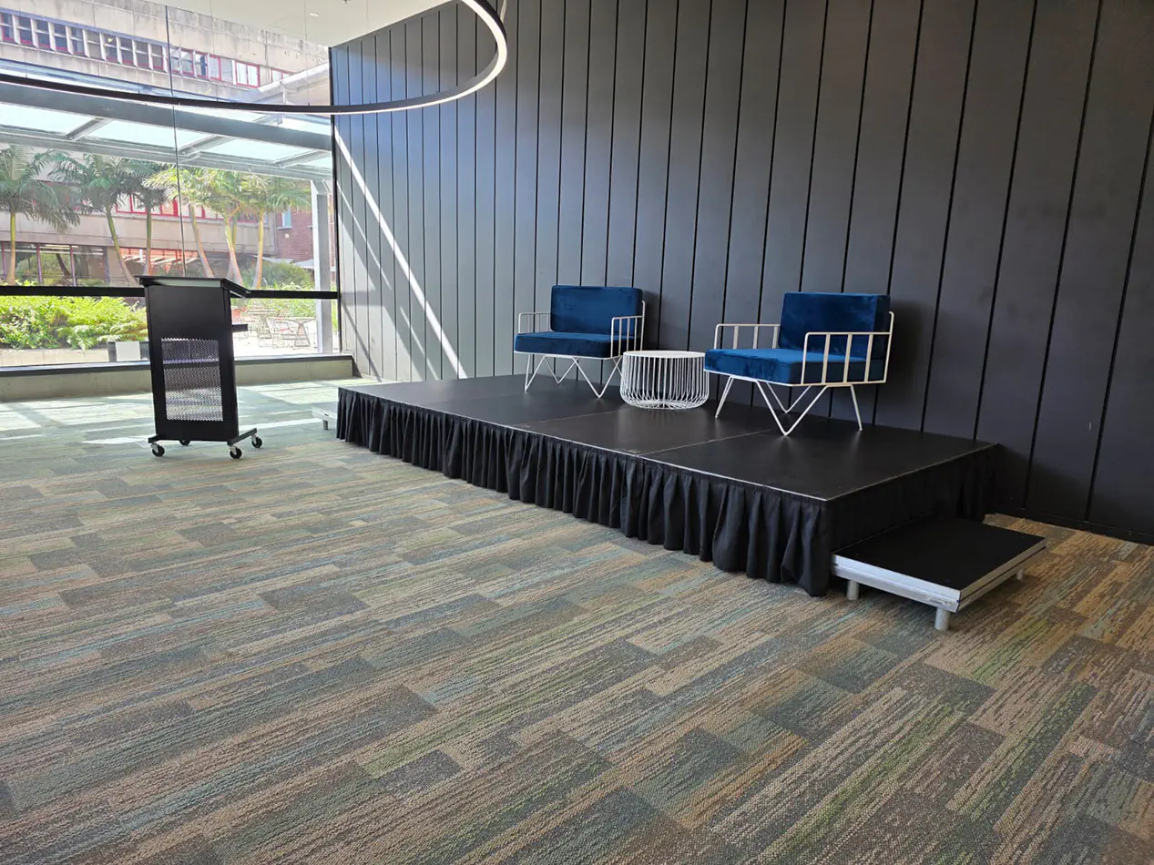 Blue velvet wire armchairs with white wire coffee table displayed on a small presentation stage beside a lectern in a conference venue
