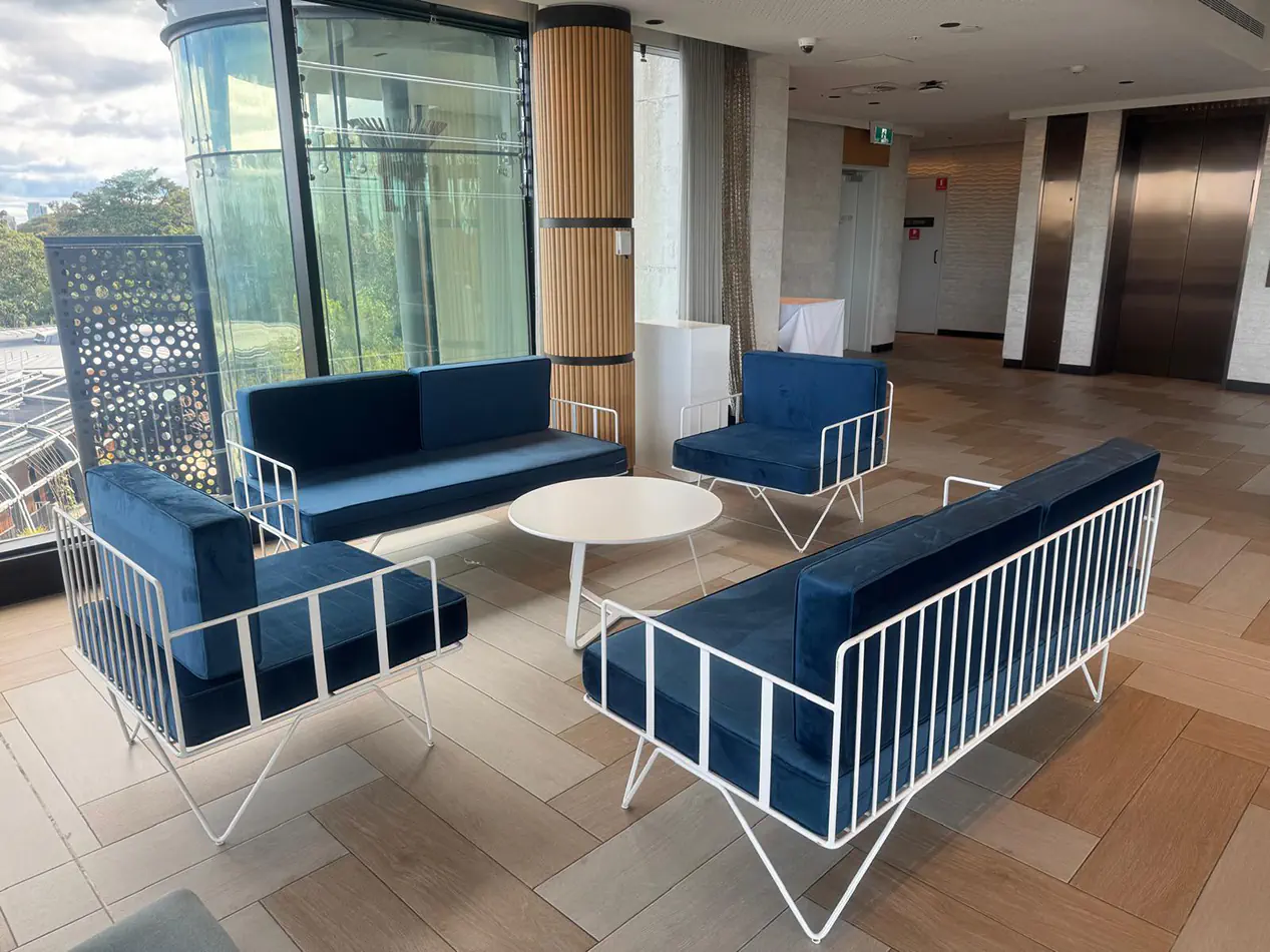 Blue velvet wire lounge seating with matching armchairs and white round coffee table arranged inside a modern function venue