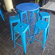 Blue wire frame cocktail table with matching blue stools arranged in a modern indoor event space with bar furniture in the background