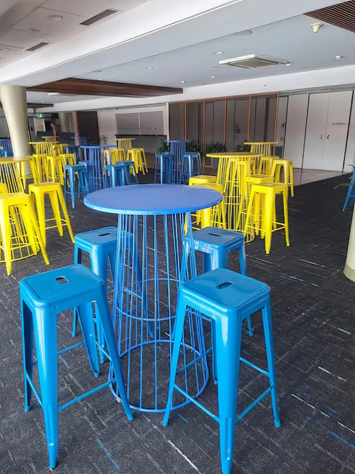 Blue wire cocktail table with matching stools used in an indoor event setup with multiple tables arranged across the venue