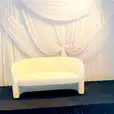 A white bouclé 2 seater sofa in front of a white backdrop.